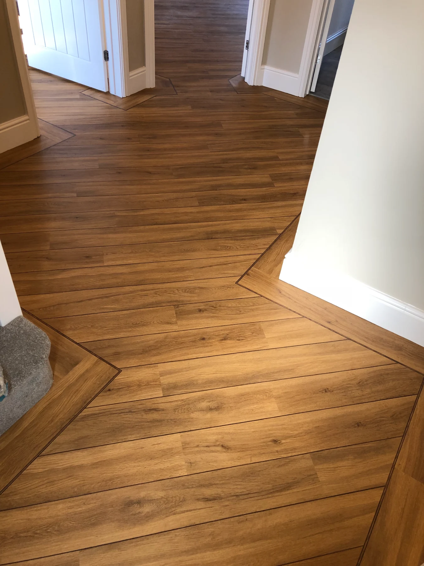 Bespoke Luxury LVT Installation with Precision Border Detailing A masterclass in luxury residential floor fitting. This project features a premium Wood-Effect Luxury Vinyl Tile (LVT) floor, completely transformed by laying the master planks on a dynamic 45-degree angle to create an incredible sense of space and architectural flow throughout the hallway.  To elevate the finish to absolute showroom standards, our fitters hand-cut and installed a crisp, dark feature border strip tracking the entire perimeter. Scribing a straight border perfectly against complex, multi-angled timber skirtings and doorway architraves requires elite carpentry skills, resulting in a completely flush, premium border frame.  Flooring Type: Premium Wood-Effect LVT (Luxury Vinyl Tile)  Design Pattern: 45-Degree Diagonal Plank with Custom Feature Border Strips  Key Craftsmanship: Complex architrave scribing & flawless diagonal layout alignment  Location: South Wales Installation Service