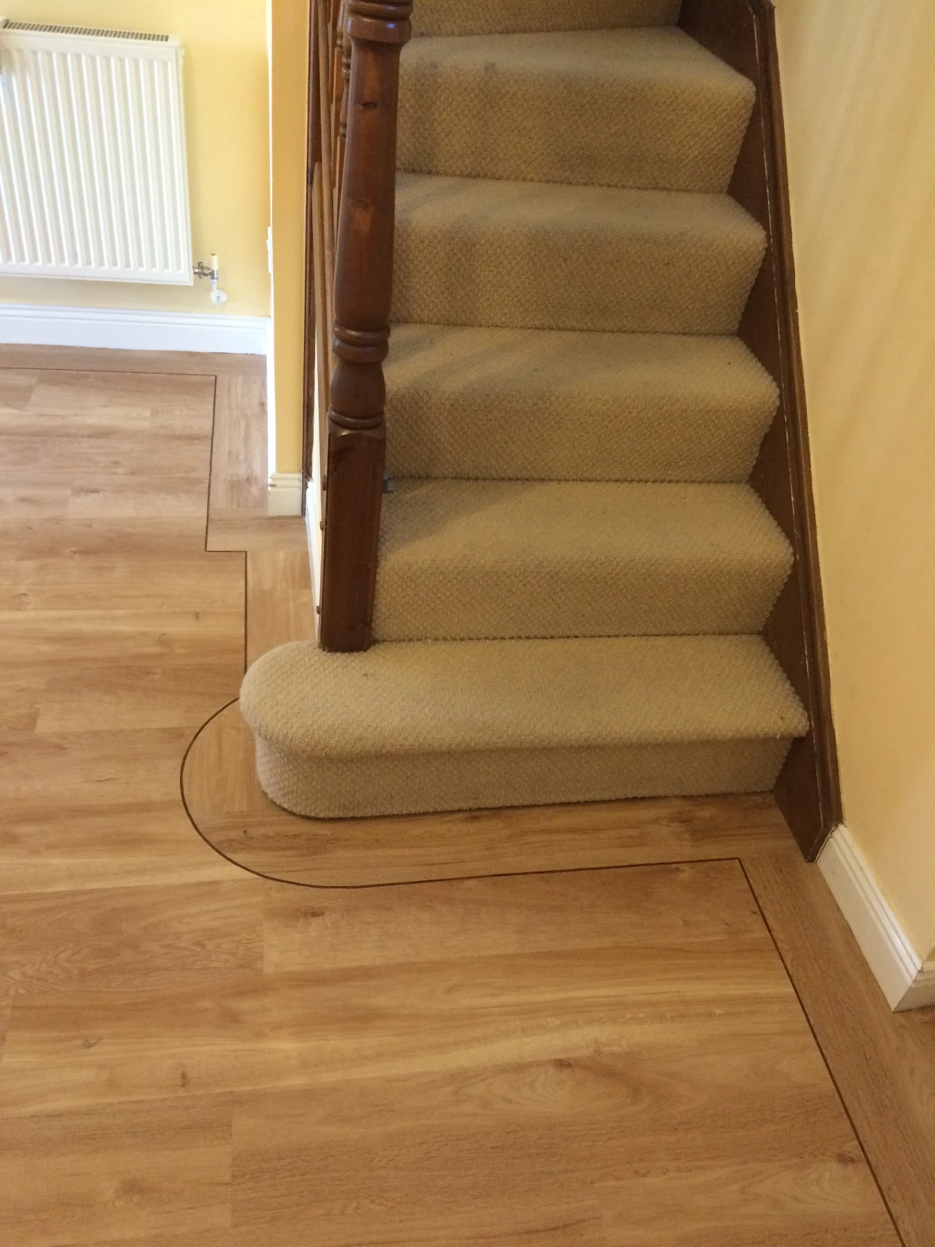 Bespoke LVT Border Work & Bullnose Staircase Integration A stunning showcase of precision craftsmanship completed by our expert installation team. This project required a seamless, high-end transition between a premium Wood-Effect Luxury Vinyl Tile (LVT) ground floor and a classic neutral carpeted staircase.  The highlight of this installation is the intricate, custom-scribed dark feature strip border. It perfectly flows around the curved architecture of the initial bullnose step, highlighting the unique shape rather than hiding it. The alignment of the LVT planks against the timber skirting demonstrates flawless subfloor preparation and cutting accuracy.  By running the clean lines of the border directly into the staircase base, we created an elegant, integrated architectural feature that elevates the entire hallway.  Flooring Type: Premium Wood-Effect LVT & Neutral Twist Pile Carpet  Custom Detailing: Hand-scribed dark feature border strips  Architectural Elements: Curved bullnose step integration & precision radiator pipe profiling  Finish Level: Fully flush subfloor preparation with exact timber skirting alignment  Location: South Wales Installation Service